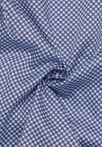 Tessuto di cotone con un motivo geometrico di cerchi intersecati in blu navy e blu chiaro su uno sfondo testurizzato.