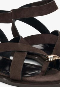 Hnědé semišové sandály s kříženými popruhy, černou stélkou a zlatým akcentem na přední části. Plná podrážka navržená pro pohodlí.