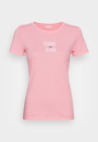 Světle růžové krátké rukávy přiléhavé tričko s bílým logem "Tommy Jeans" a malým červeným, bílým a černým designem vlajky uprostřed hrudi.