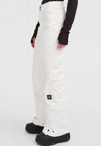 Vita snöbyxor med en elegant design, som har en hög midja, två knappar, snedställda sömmar och elastiska benslut, kombinerat med svarta stövlar.