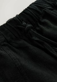 Gros plan sur un pantalon à taille élastique noire avec un cordon noué et un tissu texturé.