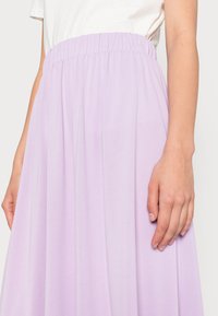 Lavendel maxi rok met een elastische tailleband, vloeiende stof en zachte textuur. Hand geplaatst bij de tailleband voor perspectief.