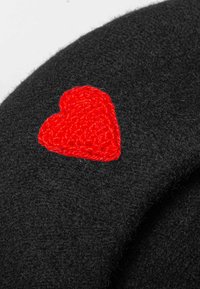 Czarna wełniana tkanina o teksturowanej powierzchni z czerwonym haftowanym sercem, które dodaje koloru projektowi.