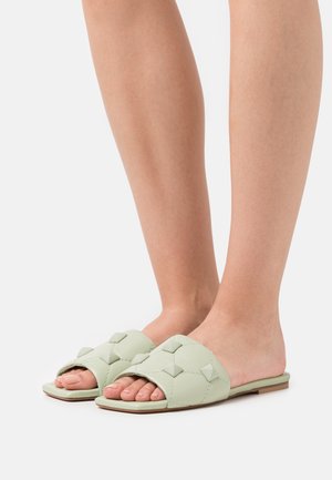 Sandales à plateforme de couleur vert clair avec un design matelassé et des clous carrés. Ouvertes à l'avant avec une semelle plate et une finition lisse.