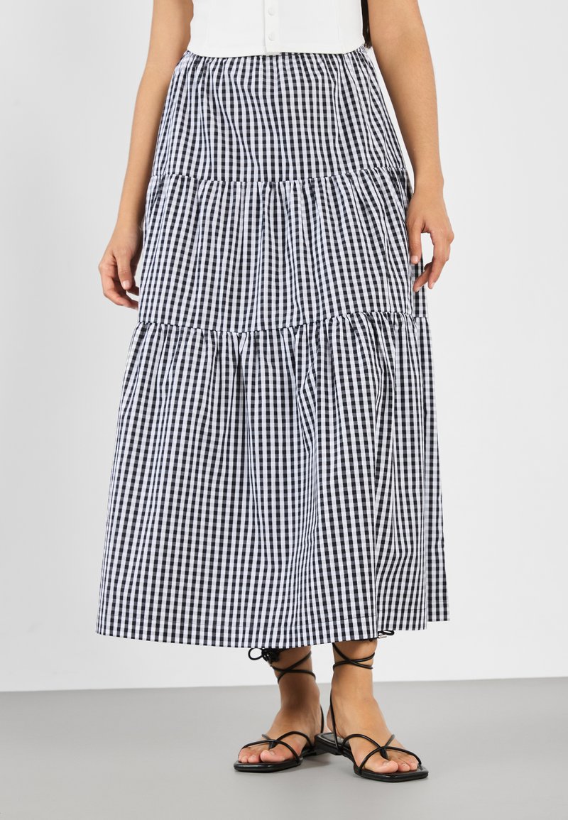 Zwart-witte geruite maxi rok, in tiered ontwerp met gathered details, gemaakt van lichtgewicht stof, gecombineerd met zwarte sandalen met bandjes.