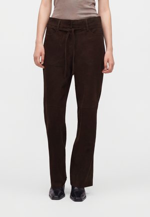 Personne portant un pantalon marron foncé à jambes droites avec une ceinture à nouer, un haut beige et des chaussures noires à bout carré.