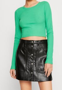 Groene geribbelde lange mouwen crop top met een ronde hals, gecombineerd met een zwarte neplederen minirok met een knoopsluiting aan de voorkant en zakken.