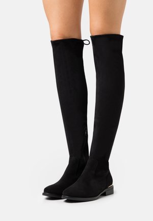 Bottes noires montantes au-dessus du genou en daim, présentant une silhouette fine, une fermeture éclair sur le côté et un petit talon bloc.