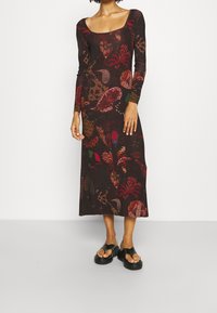 Robe à manches longues, décolletée carrée, en tissu léger à motifs, arborant des motifs floraux rouge foncé, verts et orangés, d'une longueur midi.