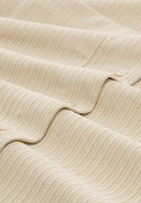 Beżowa tkanina o fakturze z prążkowanym wzorem, z delikatnym połyskiem i nierównymi fałdami. Wzdłuż krawędzi znajdują się małe guziki.