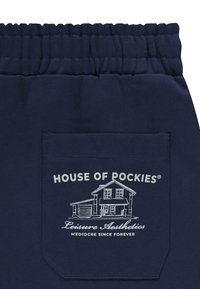 Marineblauwe sweatpants hebben een verzamelde elastische tailleband en een achterzak met witte bedrukte tekst en een architectonisch grafisch ontwerp.