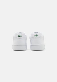 Sneaker in pelle bianca con logo di coccodrillo verde sul retro, punta tonda e colletto imbottito. Suola in gomma con dettagli di cucitura minimi.