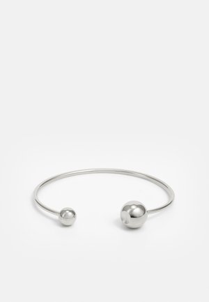 Silberner Metallarmreif mit zwei kugelförmigen Akzenten an jedem Ende, glatte Oberfläche, offenes Design und schlanker, minimalistischer Form.