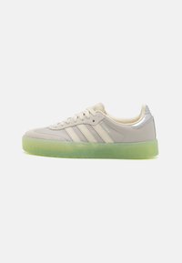 Light gray sneakers with three white stripes, textured leather, a silver accent at the heel, and a semi-transparent green rubber sole.