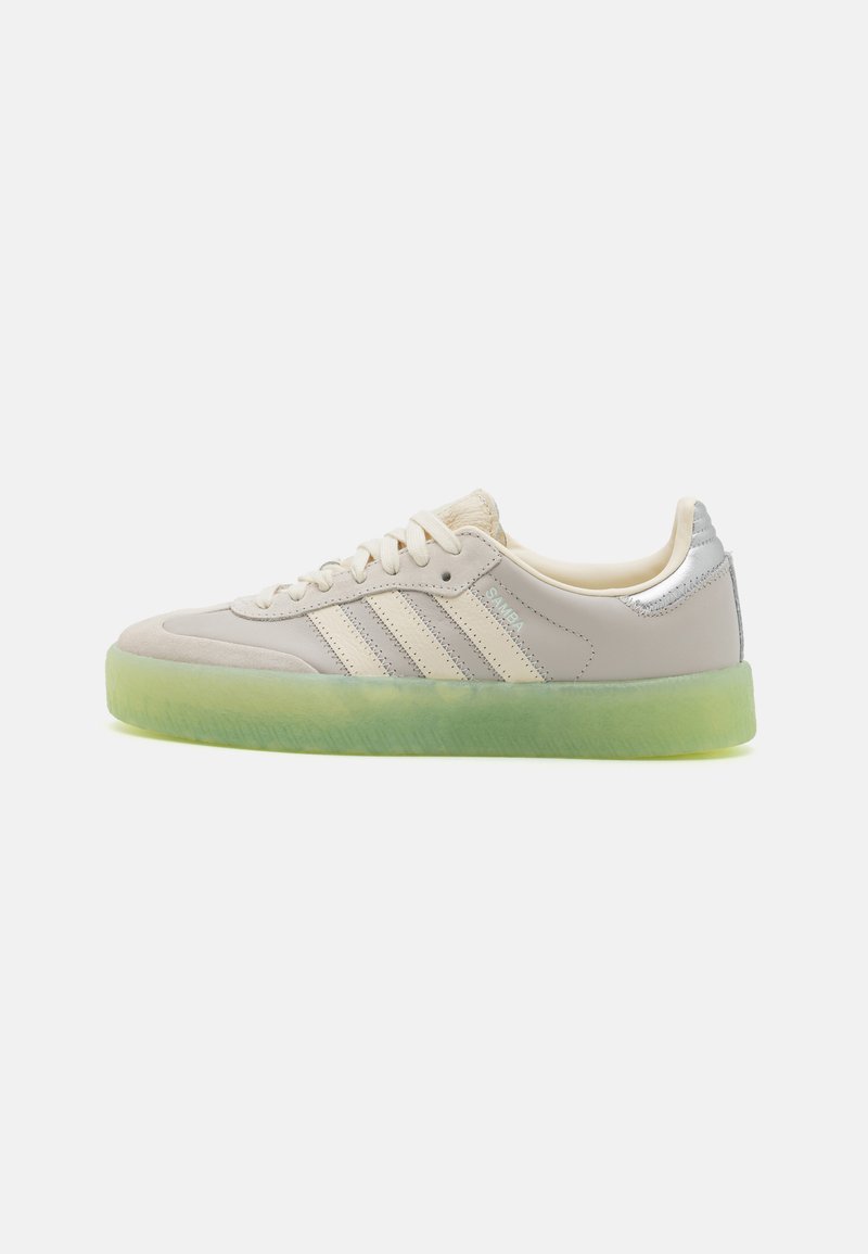 Light gray sneakers with three white stripes, textured leather, a silver accent at the heel, and a semi-transparent green rubber sole.