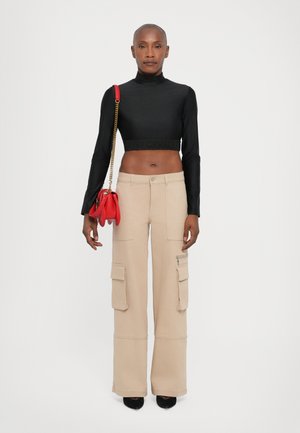 Zwarte cropped turtleneck top, beige wijde cargobroek met zakken en een rode handtas met kettingband. Zwarte hakken maken de look compleet.