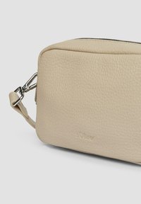 Beżowa torebka crossbody z teksturowanej skóry z srebnym zapięciem i zamkiem, z wytłoczonym logo s.Oliver z przodu, na jednolitym tle.