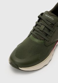 Grüne Mesh-Sneaker mit strukturierten Oberflächen, ausgestattet mit einer Schnürung und einer weichen, gepolsterten Sohle. Der Markenname "Tamaris" ist sichtbar.