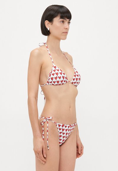 Bikini set featuring white fabric with red heart patterns, triangular top with ties, and low-rise bottom with side ties.