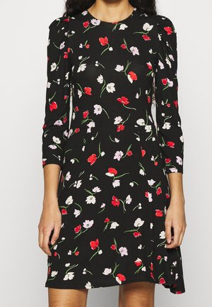 Zwarte jurk met rood, wit en roze bloemenprint, driekwart pofmouwen en een getailleerde taille, gedragen door een persoon met lang krullend haar.