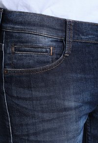 Mörkblå denimjeans med slim fit, som har en bakficka med sömdetaljer och en jämn textur. Tyget har en lätt lyster.