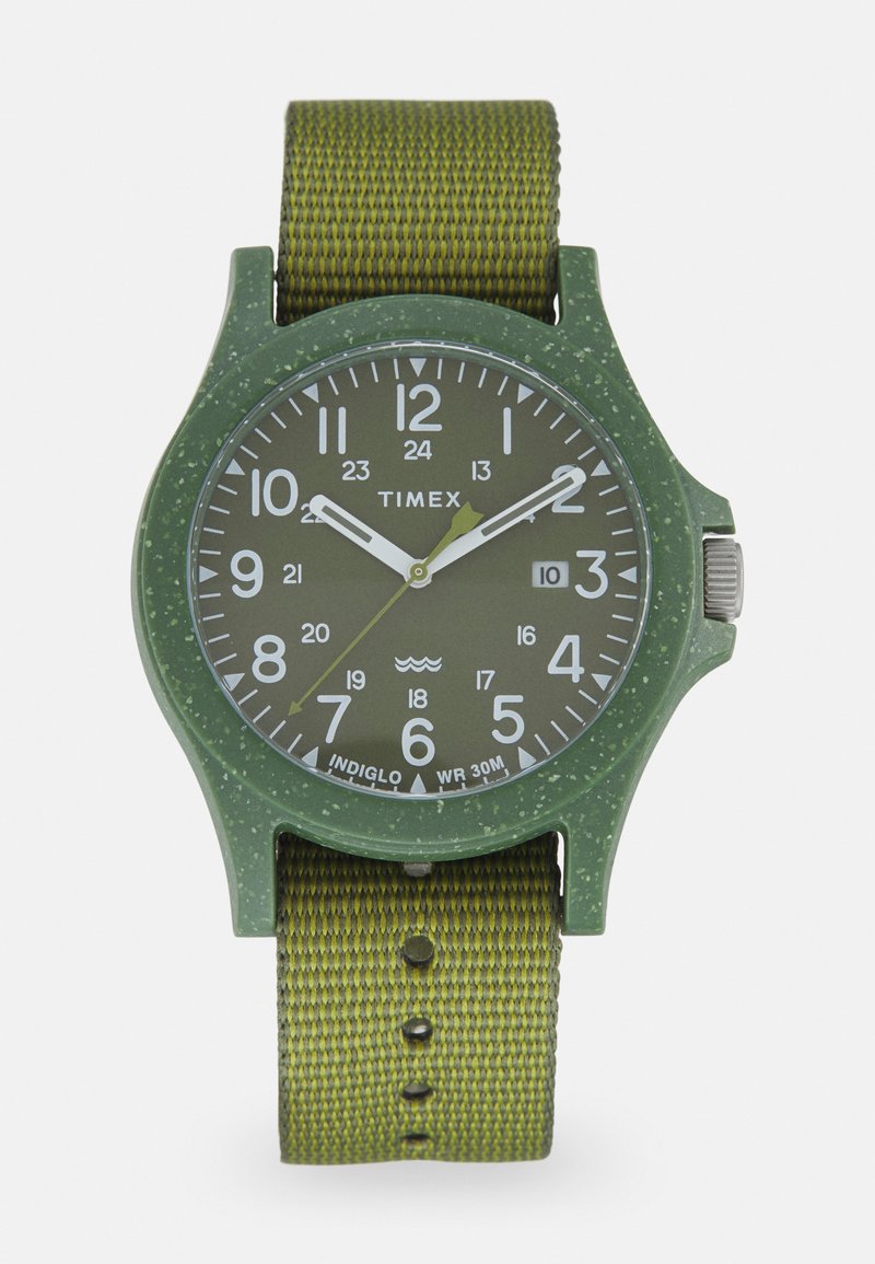 Timex-Uhr mit einem grünen Kunststoffgehäuse, weißen Ziffern und einem strukturierten grünen Nylonarmband. Verfügt über Indiglo-Beleuchtung und eine Wasserfestigkeit von 30 m.