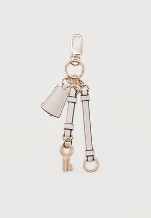 Μπρελόκ με χρυσό κούμπωμα, δύο λευκά δερμάτινα λουράκια, μικρή λευκή υφασμένη ετικέτα και χρυσό διακοσμητικό κλειδί σε απλό φόντο.