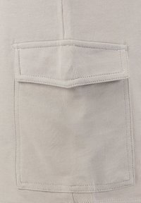 Tissu gris clair montrant une poche plate avec un rabat droit, des coutures plates et une texture lisse, conçu pour un usage fonctionnel.