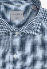 Camisa slim fit de tejido entrelazado con un patrón de líneas cruzadas en azul marino y blanco. Incluye un botón blanco y una etiqueta en el cuello.