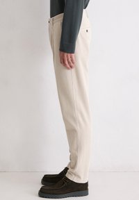 Pantalons en velours côtelé beige avec des côtes verticales, coupe droite et poches latérales. Associés à des chaussures en daim marron foncé.