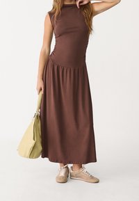 Ruskea hihaton mekko rypytetystä bodysta ja valuva hameosa. Yhdistetty beigeihin lenkkareihin ja vaaleanvihreään olkalaukkuun. Sileä pinta.