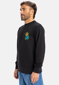 Black sweatshirt with long sleeves, round neckline, featuring a turquoise and yellow graphic design on the chest. Soft texture, casual fit.