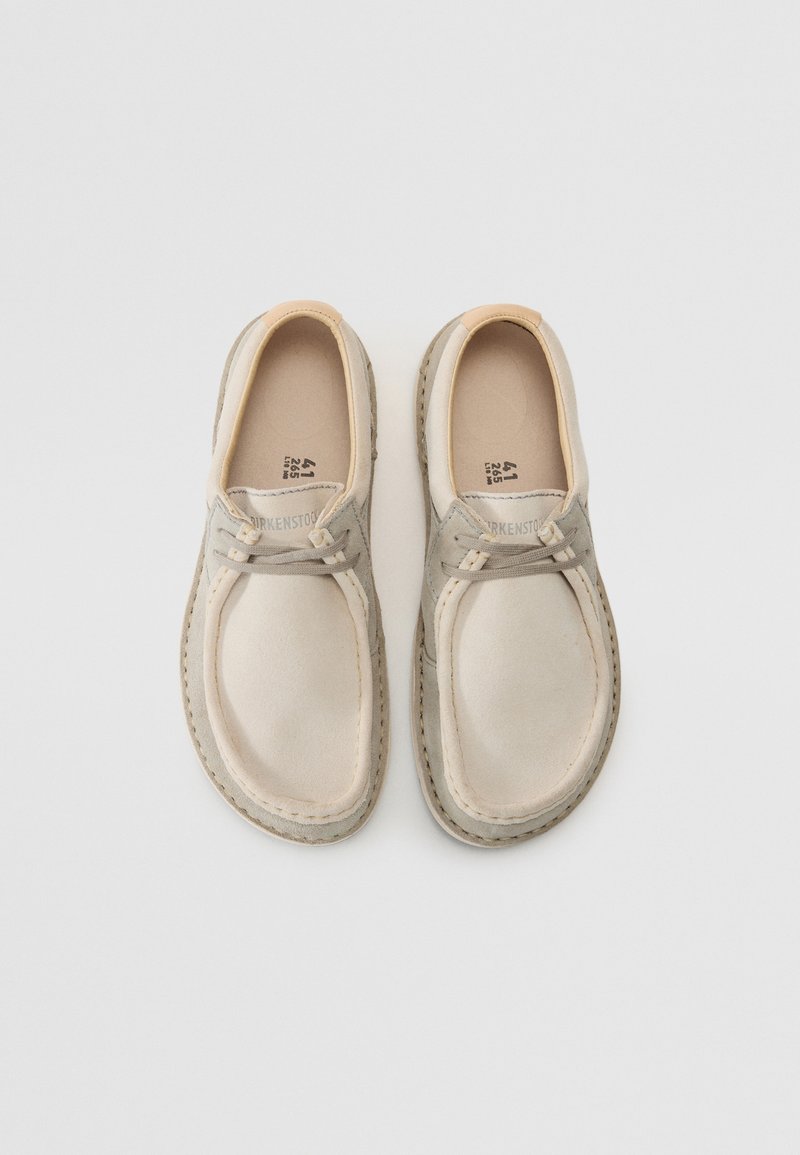 Jasno-beżowe buty wsuwane z ciemno-beżowymi akcentami, miękka zamszowa faktura, okrągły czubek i widoczne przeszycia wzdłuż podeszwy.