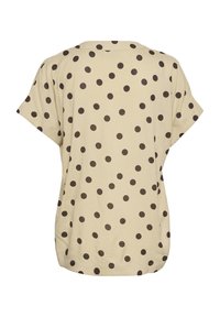 Haut beige à manches courtes avec des pois noirs, coupe ample, encolure ronde et ourlet légèrement incurvé.