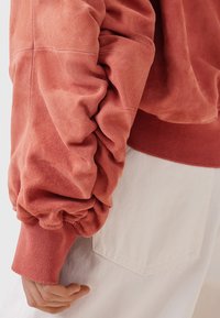 Roestkleurig suede sweatshirt met gathered mouwen en geribde manchetten. De stof lijkt zacht met een textuur die doet denken aan geborsteld suede.