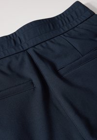 Pantalon en tissu bleu marine avec une texture lisse, une ceinture élastique et deux poches arrière ornées d'une couture subtile.