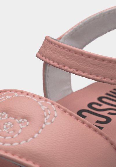 Ροζ δερμάτινο λουράκι σανδαλιού με ραφές σε σχήμα λευκής αρκούδας και μέρος μαύρου κειμένου εμπορικής επωνυμίας στην εσωτερική σόλα, στενή οπτική γωνία.