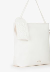 Witte nep-lederen totebag met een textuur van een bloemenpatroon aan één kant, enkele schouderriem en het gouden V73-logo aan de onderkant.