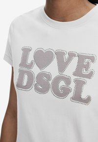 Maglietta in cotone bianco con la scritta "LOVE DSGGL" in grassetto grigio, impreziosita da dettagli metallici a borchie attorno al testo.
