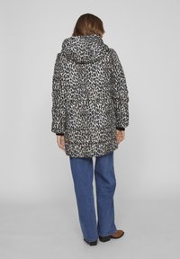 Chaqueta acolchada con un diseño de estampado de leopardo, capucha y puños acanalados. Combinada con jeans de tiro alto de pierna ancha azules y botas de tobillo marrones.