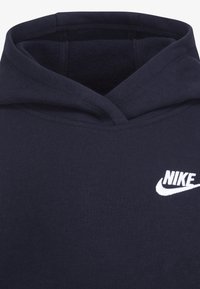 Sötétkék pulóver puha szövetből, bordázott aljjal. A mellkasán fehér Nike logó található, és zsinórral ellátott kapucnival készül.