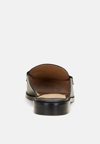 Sandal de couro preto com acabamento liso, com as costas abertas e bico quadrado. Apresenta um interior castanho claro e um salto baixo e retangular.