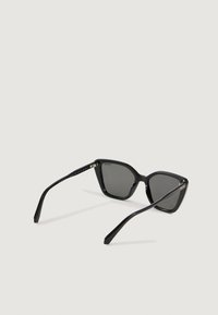 Mustat kissansilmäaurinkolasit tummilla polarisoiduilla linsseillä avoimena vaalealla pinnalla.