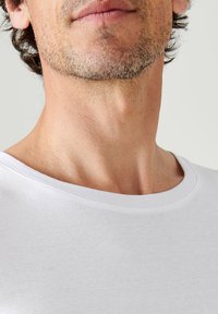 T-shirt bianca con scollo rotondo ampio, realizzata in morbido cotone. Il colletto ha una finitura semplice e pulita con una leggera texture.