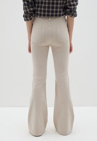 Beige flared pants met een gladde textuur, hoge taille en twee achterzakken. Het ontwerp biedt een getailleerde look bij de taille, terwijl het uitloopt bij de enkels.