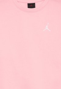 Rosa crewneck T-skjorte med hvit Jumpman-logo brodert på øvre venstre bryst og en svart Jordan-merkelapp inni kragen.