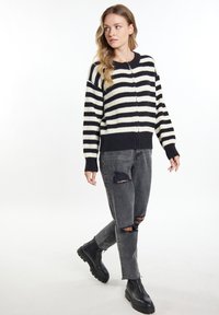 Gestreifter Strickpullover in Schwarz und Elfenbein, mit Reißverschluss vorne, gerippten Bündchen und Saum. Kombiniert mit verwaschenen schwarzen Jeans und schwarzen Chelsea-Stiefeln.