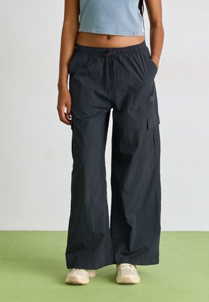 Pantaloni cargo neri, leggeri, con vita elastica, tasche laterali e vestibilità rilassata, abbinati a scarpe da ginnastica beige.