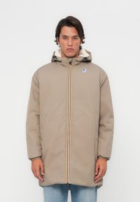 Beige hooded jack met een ritssluiting aan de voorkant, meerkleurige ritssluitingaccenten en een zachte, gevoerde binnenkant. Twee zijzakken en elastische manchetten.