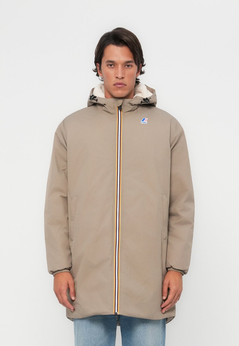 Beige hooded jack met een ritssluiting aan de voorkant, meerkleurige ritssluitingaccenten en een zachte, gevoerde binnenkant. Twee zijzakken en elastische manchetten.